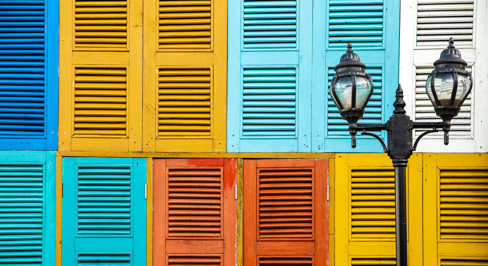 Two-light street lamp with colorful window background.