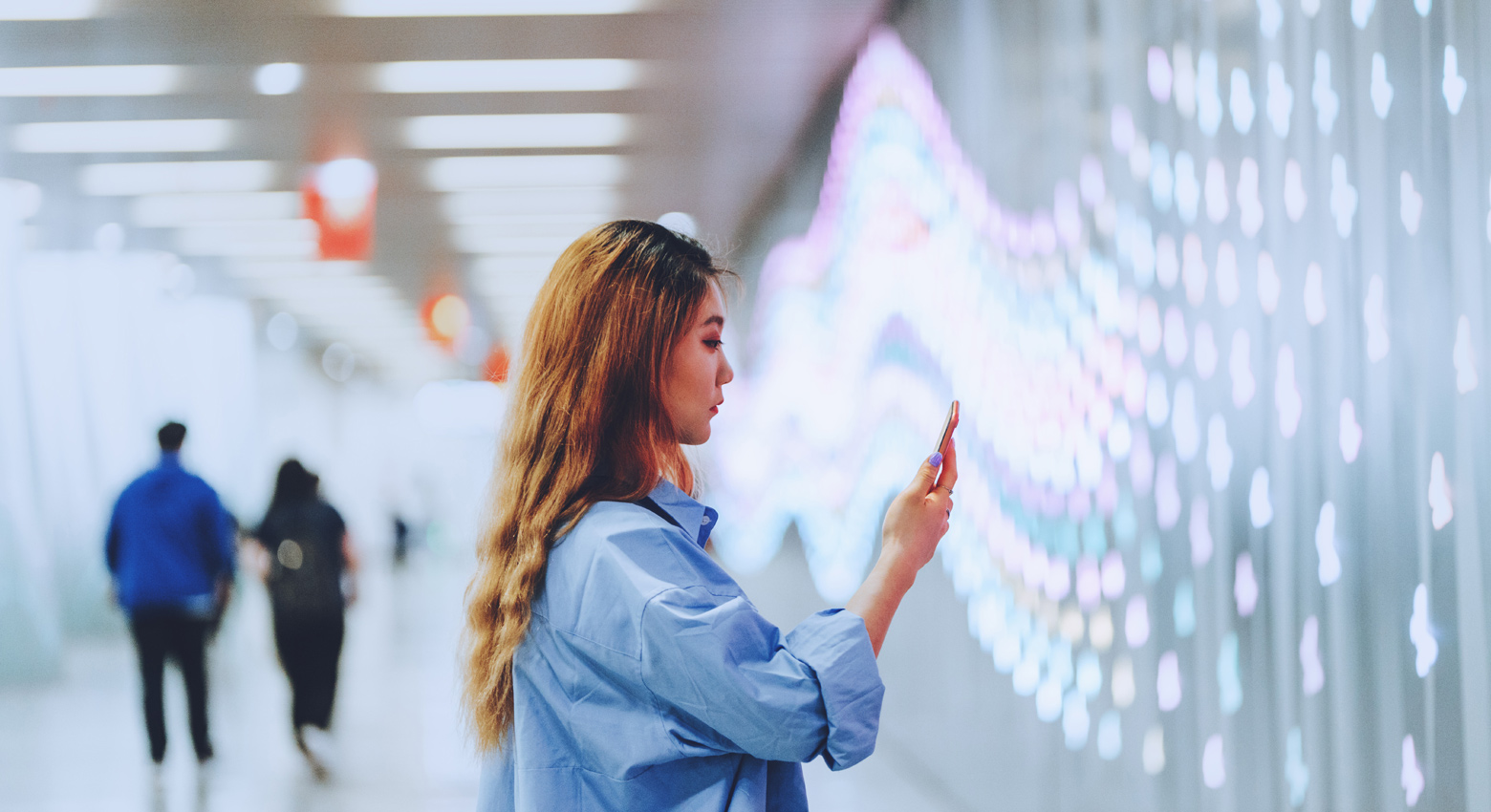 Woman looking at phone in front of wall of lights 