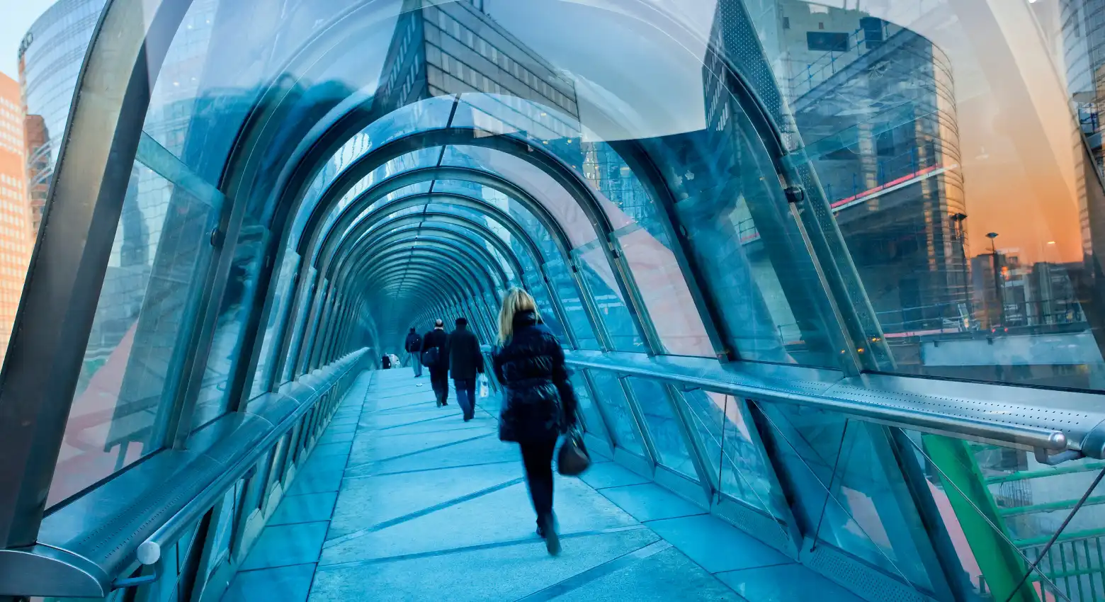 People walking on bridge between modern architecture 