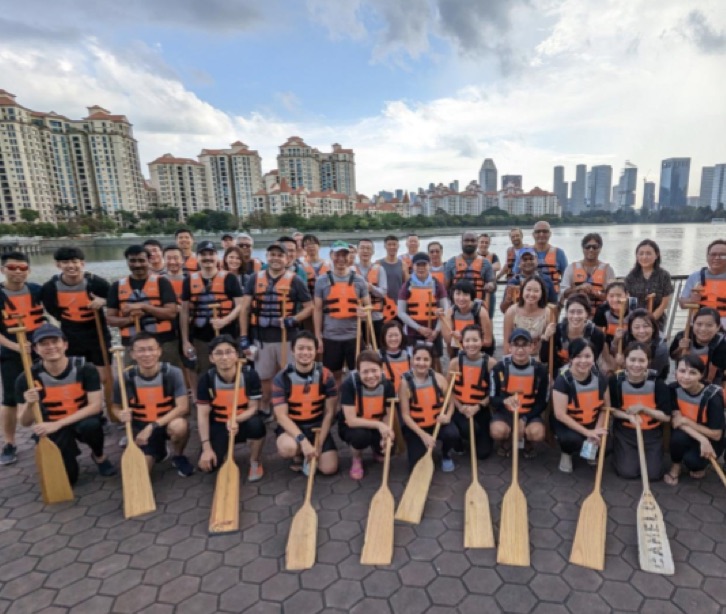 Group of employees in life jackets holding boat paddles in front of a lake