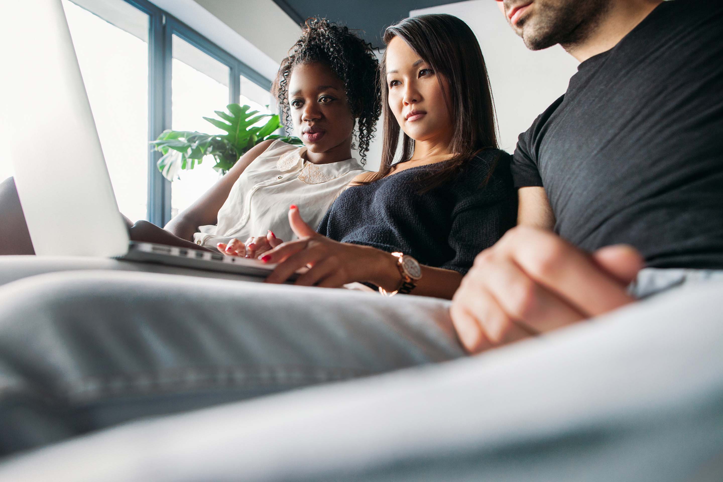 Three colleagues sitting on a couch looking at a laptop screen