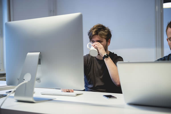 Person taking a drink of coffee from a white coffee mug while they are working on their desktop